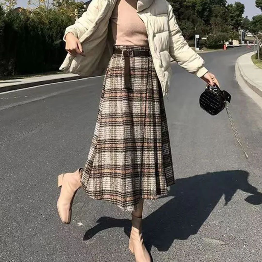 Frau in kariertem Rock, beiger Jacke und Stiefeletten auf Straße, modisch, Herbstmode.