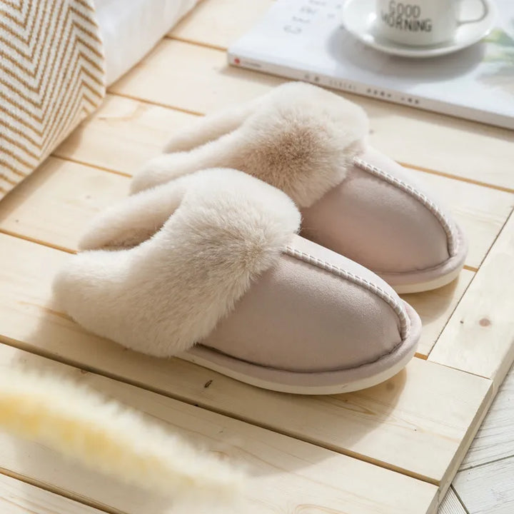 Beige Hausschuhe aus Kunstfell, gemütlich, rutschfest, ideal für den Winter, auf Holzuntergrund.
