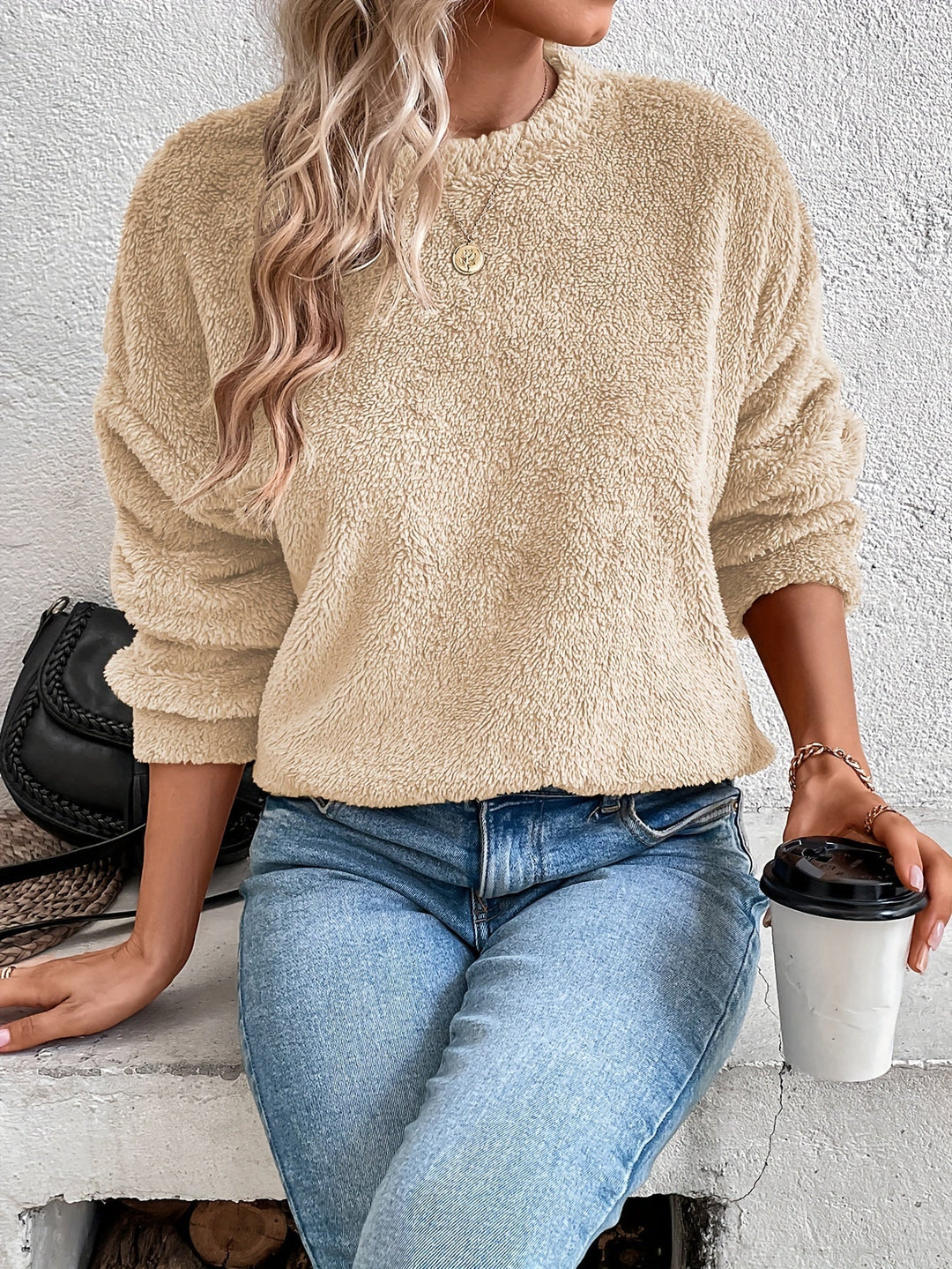 Frau in beigem Fleece-Pullover, blaue Jeans, hält Kaffeebecher, modisch, lässiger Look.