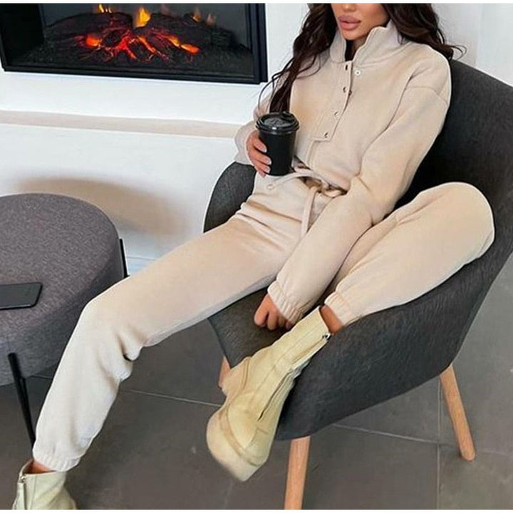 Frau in beigem Jogginganzug, sitzt auf Stuhl, hält Kaffeetasse, gemütliche Wintermode.