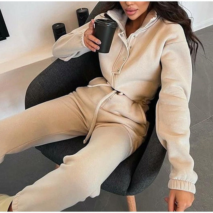 Frau in beigem Jogginganzug mit Kaffeetasse, gemütliche Lounge-Mode, modernes Wohnzimmer.