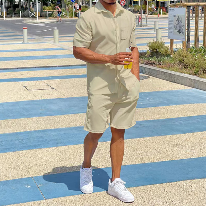 Mann in beigem Kurzarm-Overall mit Getränk, weiße Sneaker, Sommermode, urbaner Hintergrund.