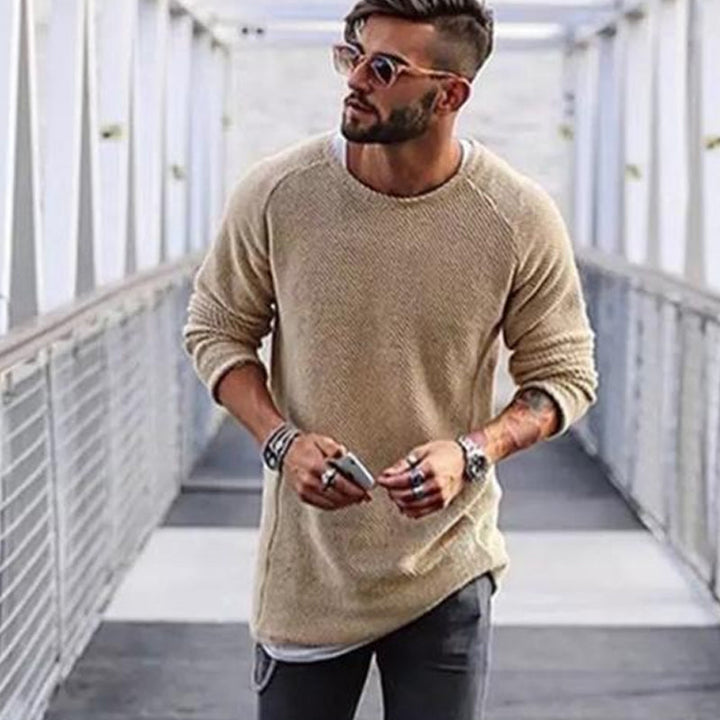 Mann mit beigem Strickpullover, Sonnenbrille und Armbändern auf Brücke, modischer Herrenstil.