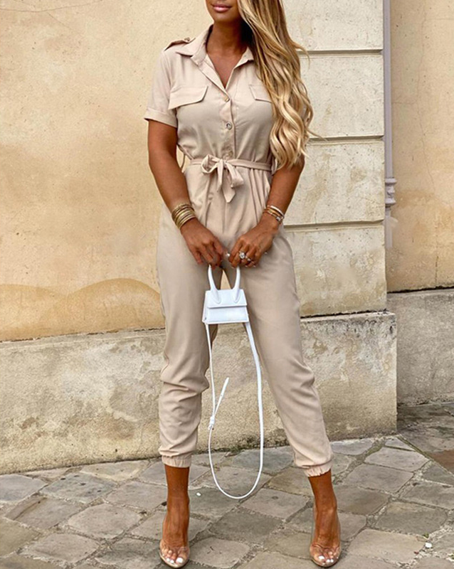 Frau in beige Jumpsuit mit Gürtel, langen Ärmeln, Knopfleiste, vor beiger Wand.