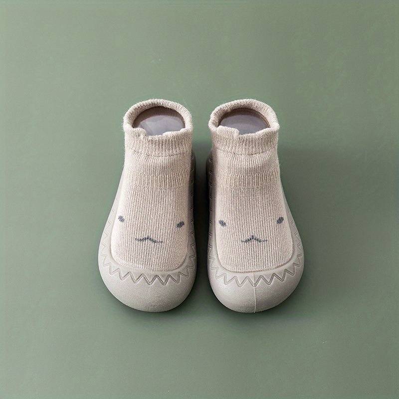 Beige Babyschuhe mit Tiergesicht, rutschfest, weiche Sohle, für Kleinkinder, auf grünem Hintergrund.