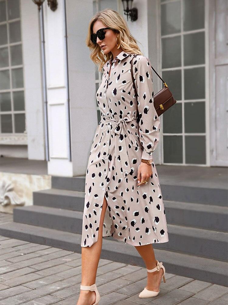 Frau in beigem, gepunktetem Kleid, Sonnenbrille, braune Tasche, elegante Mode, Stadtstraße.