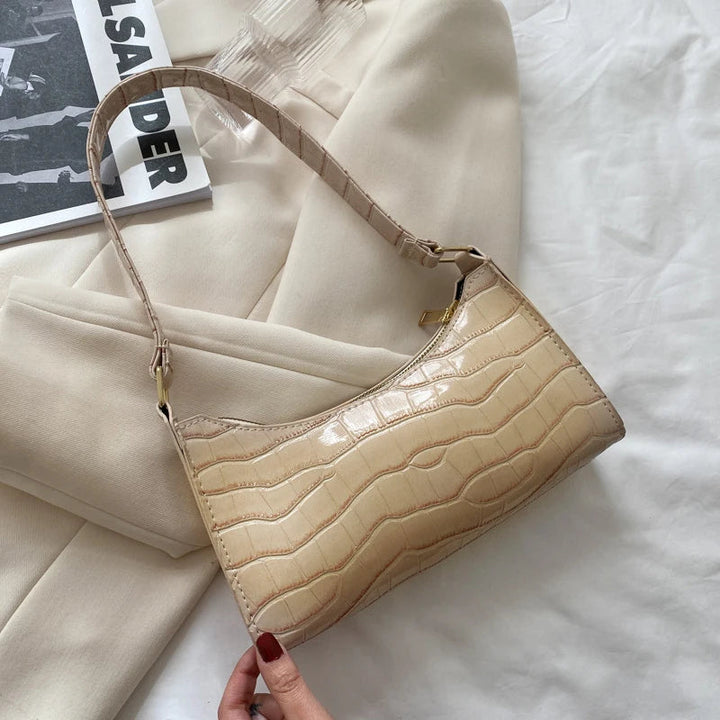 Beige Krokodilleder-Handtasche auf beigem Stoff, elegantes Design, modisches Accessoire.