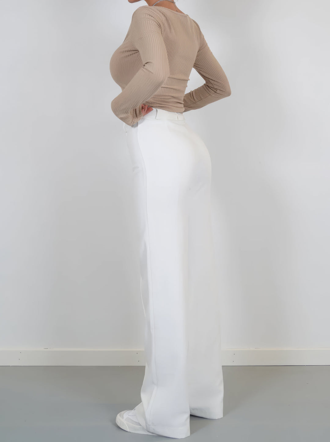 Frau in beigem Langarmshirt und weißer Hose, seitlich, Mode, Damenbekleidung, elegant.