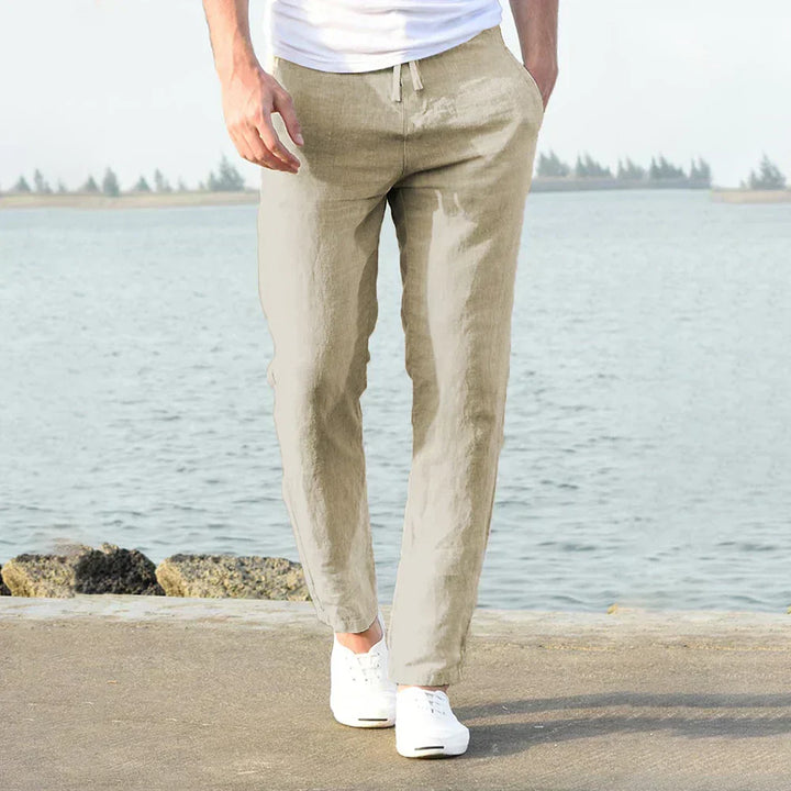Mann in beigen Leinenhosen am Wasser, lässiger Sommerstil, weiße Sneaker.