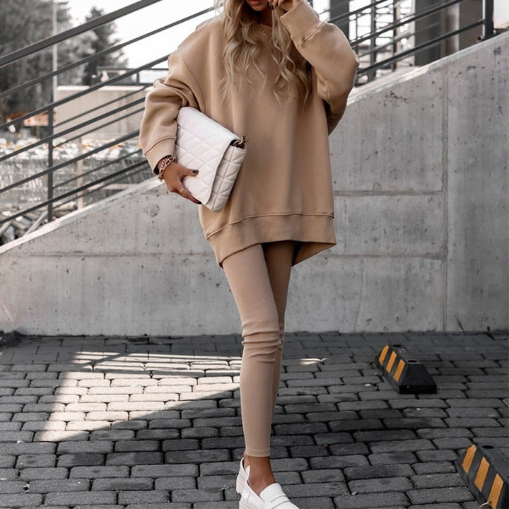 Frau in beigem Oversize-Pullover und Leggings, hält weiße gesteppte Clutch, modisch, urban.