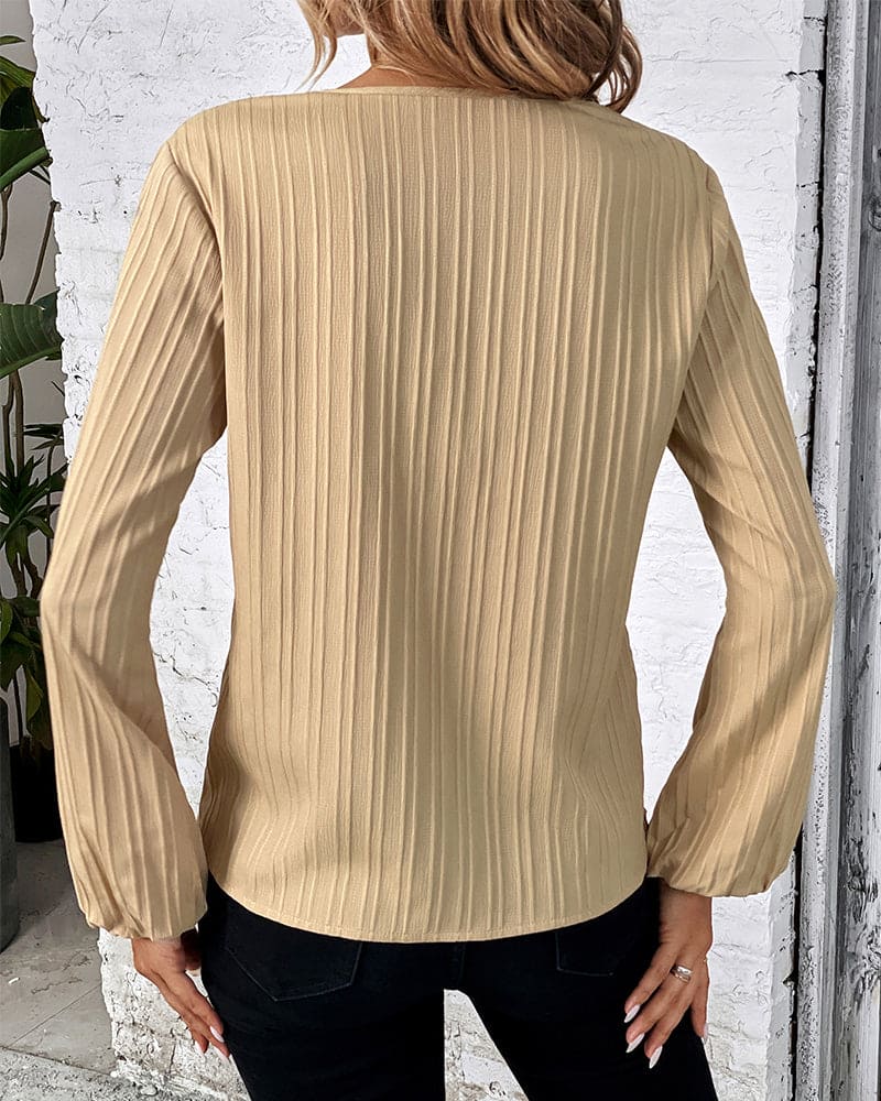 Frau in beige gerippter Bluse, Rückansicht, modisch, langärmelig, vor weißer Wand.