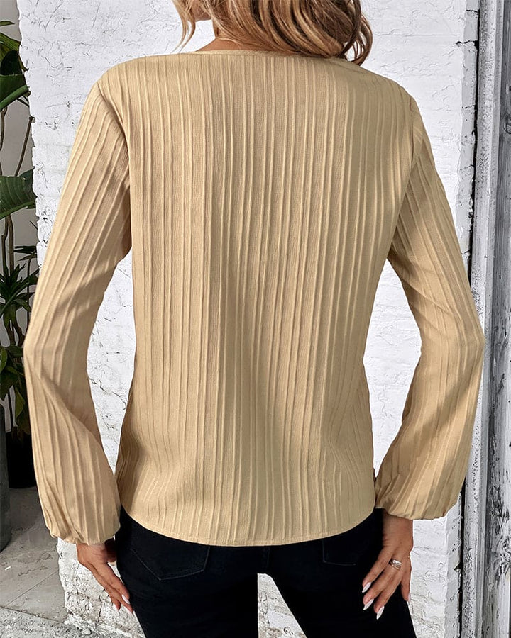 Frau in beige gerippter Bluse, Rückansicht, modisch, langärmelig, vor weißer Wand.