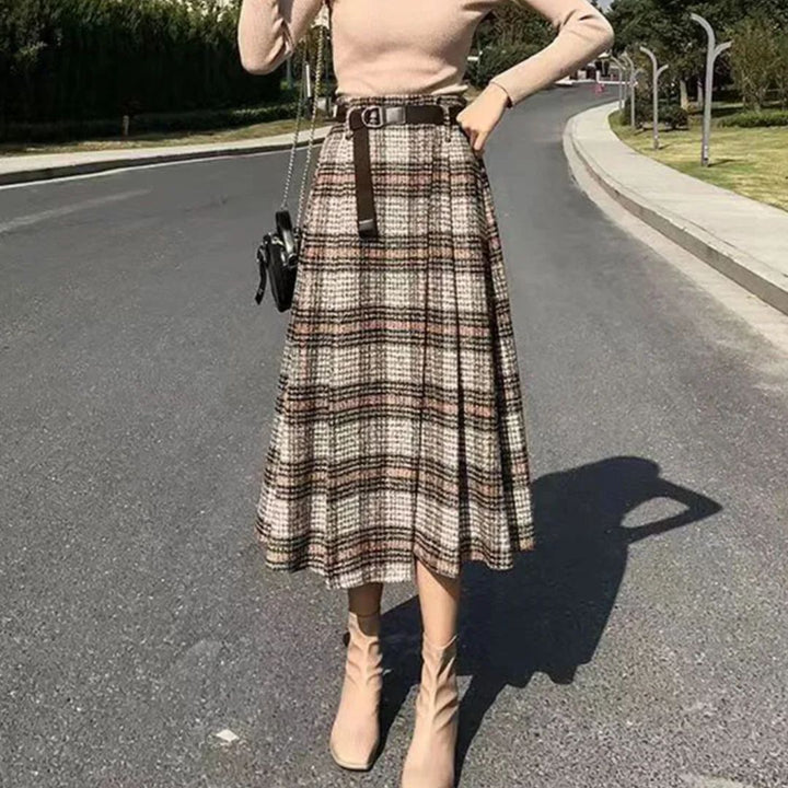 Damenmode: Kariertes Midirock-Outfit mit Gürtel, beige Stiefeletten, Straße im Hintergrund.
