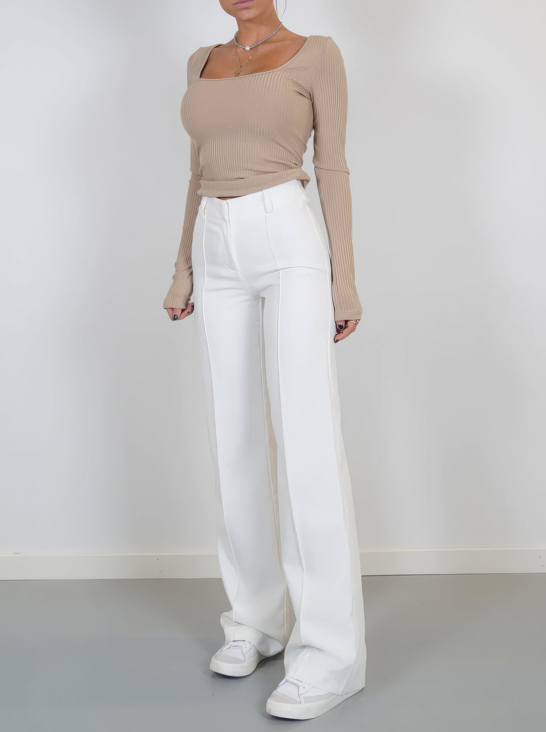 Frau in beigem Langarmshirt und weißen Schlaghosen, modisch, elegant, minimalistisch.