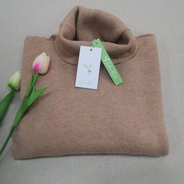 Beigefarbener Rollkragenpullover aus Kaschmir mit Etikett, neben zwei Tulpen auf beigem Hintergrund.