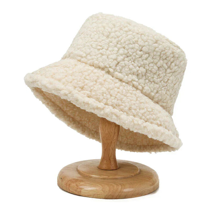 Beiger Damen-Bucket-Hut aus Fleece auf Holzständer, modisch und warm.