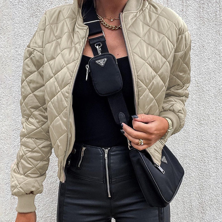 Frau in beiger Steppjacke, schwarzer Hose, mit schwarzer Umhängetasche und Handyhülle.