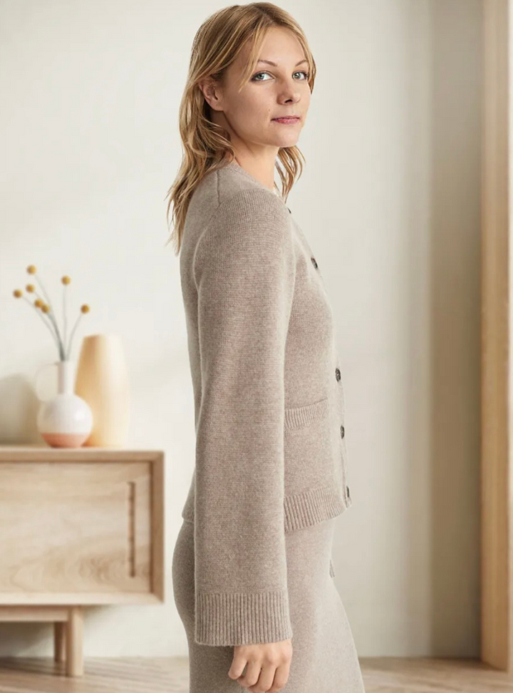 Frau trägt beige Strickjacke mit Knöpfen, weiches Material, elegantes Design, Innenraum.