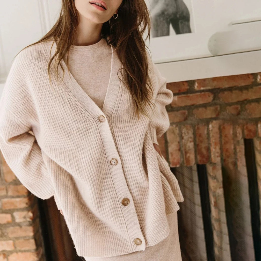 Frau trägt beige Strickjacke aus Wolle vor Kamin, modisch, gemütlich, Herbstmode.
