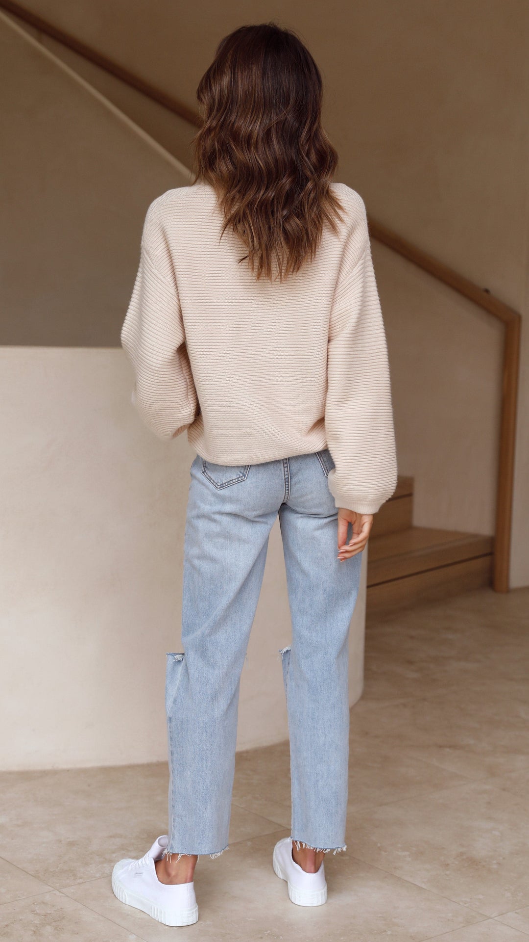 Frau in beiger Strickpullover und blauer Jeans, Rückansicht, modisch, lässiger Stil.