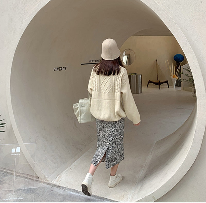 Frau in beigem Pullover und gemustertem Rock, beige Hut, weiße Tasche, Vintage-Mode.