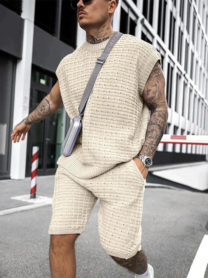 Mann in beigem Strick-Set, ärmelloses Oberteil und Shorts, modisch, urbaner Stil.