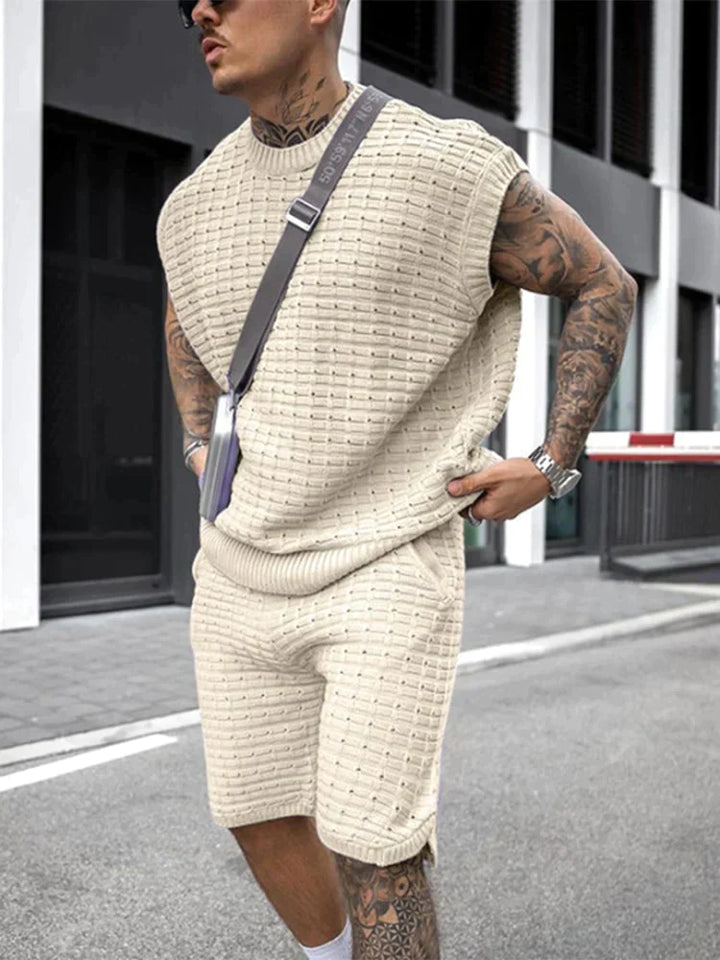Mann in cremefarbenem Strick-Set, ärmelloses Oberteil und Shorts, urbaner Stil, Sommermode.
