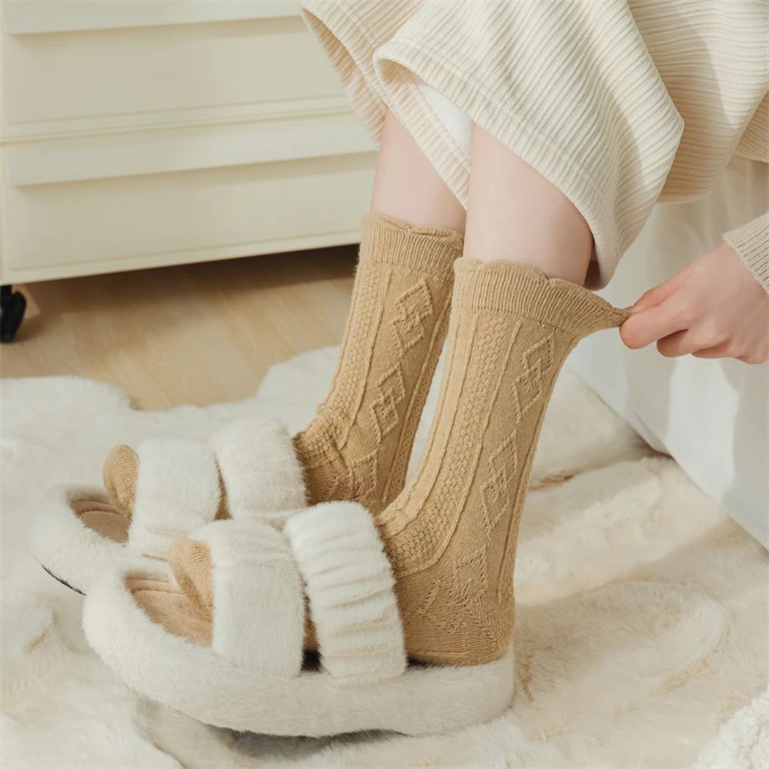 Beige Wollsocken mit Rautenmuster, getragen mit weißen Plüschsandalen auf Teppich.