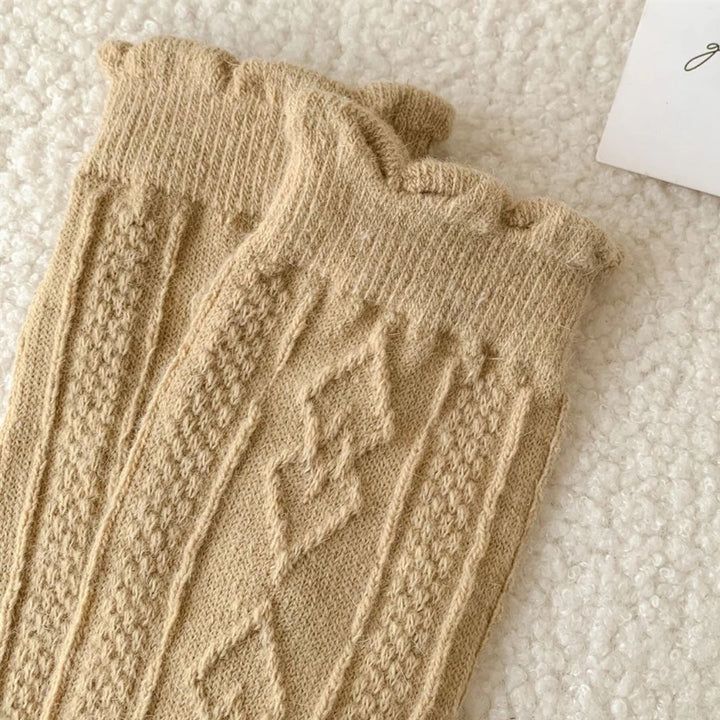 Beige gestrickte Wollsocken mit Zopfmuster auf weißem Hintergrund.