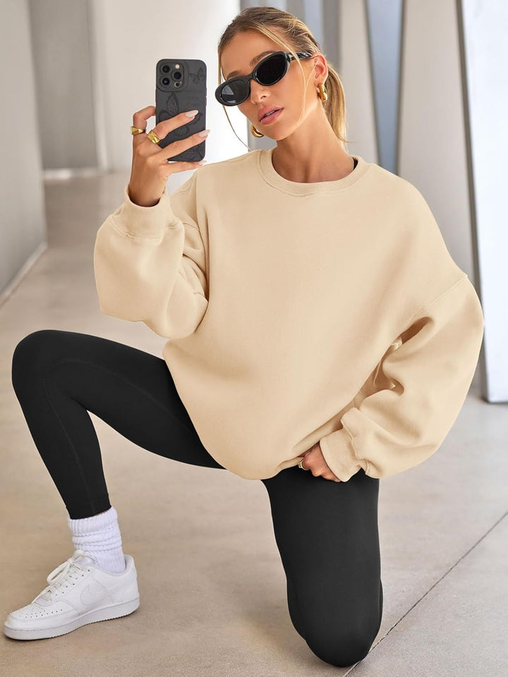 Frau in beigem Oversize-Pullover, schwarze Leggings, weiße Sneaker, Sonnenbrille, Selfie.