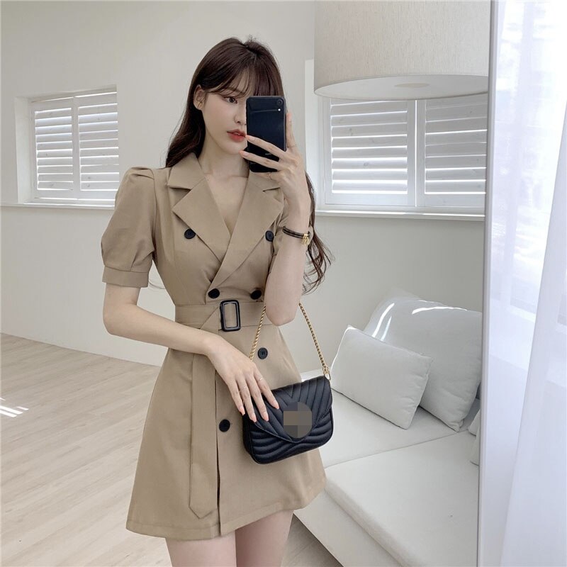 Frau in beigem Trenchcoat-Kleid mit schwarzer Umhängetasche, modernes Wohnzimmer.