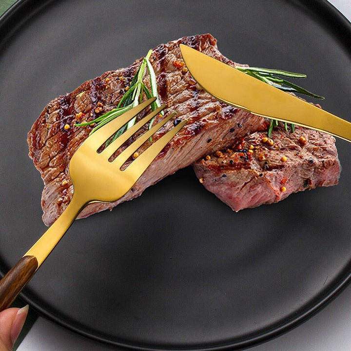 Goldenes Besteckset mit Holzgriff, Edelstahl, Messer und Gabel, auf schwarzem Teller mit Steak.