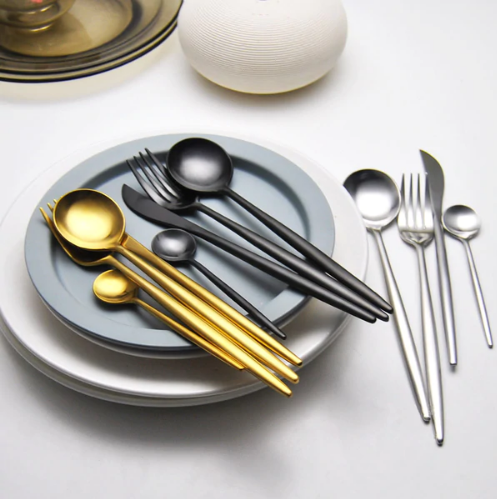 Goldenes, schwarzes und silbernes Besteck-Set auf Tellern, modernes Design, Edelstahl.