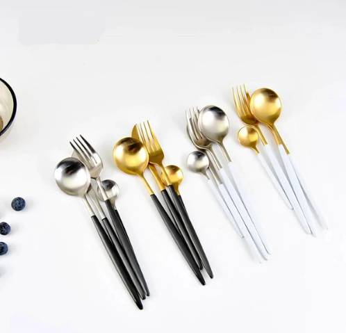 Moderne Besteckset aus Edelstahl, gold und silber, mit schwarzen und weißen Griffen, elegant.