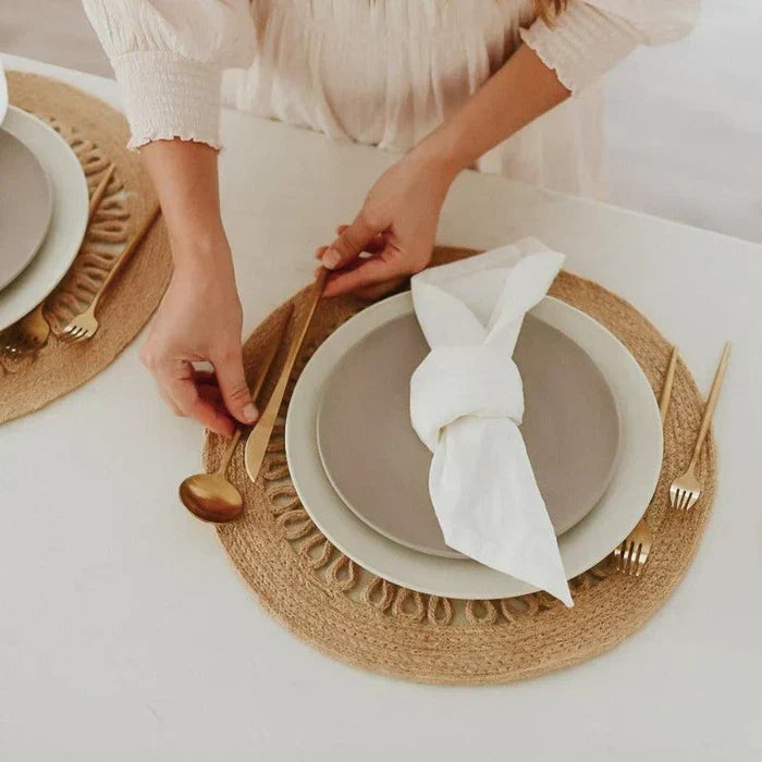 Frau arrangiert minimalistisches Besteck auf Tischset aus Jute, goldene Löffel und Gabeln.
