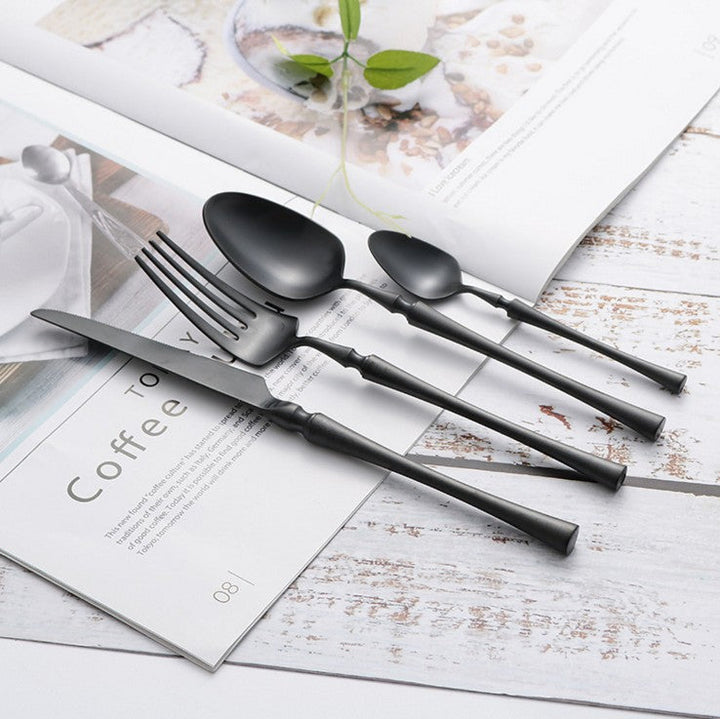 Schwarzes Edelstahl-Besteckset auf Holztisch, modernes Design, Gabel, Messer, Löffel.