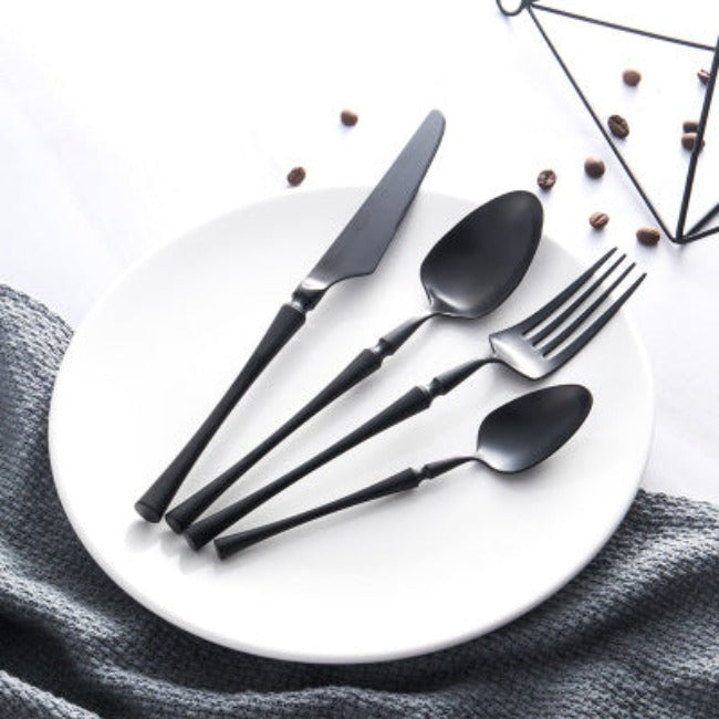 Schwarzes Edelstahl-Besteckset auf weißem Teller, modernes Design, Essbesteck.