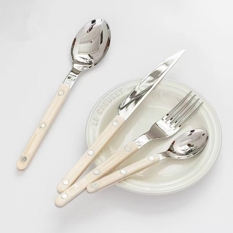 Besteckset mit weißem Griff auf Le Creuset Teller, Edelstahl, modern, elegant, Essbesteck.