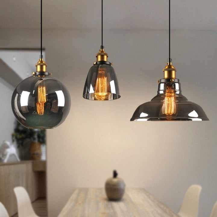 Drei moderne Pendelleuchten aus Glas mit Edison-Glühbirnen über einem Holztisch.