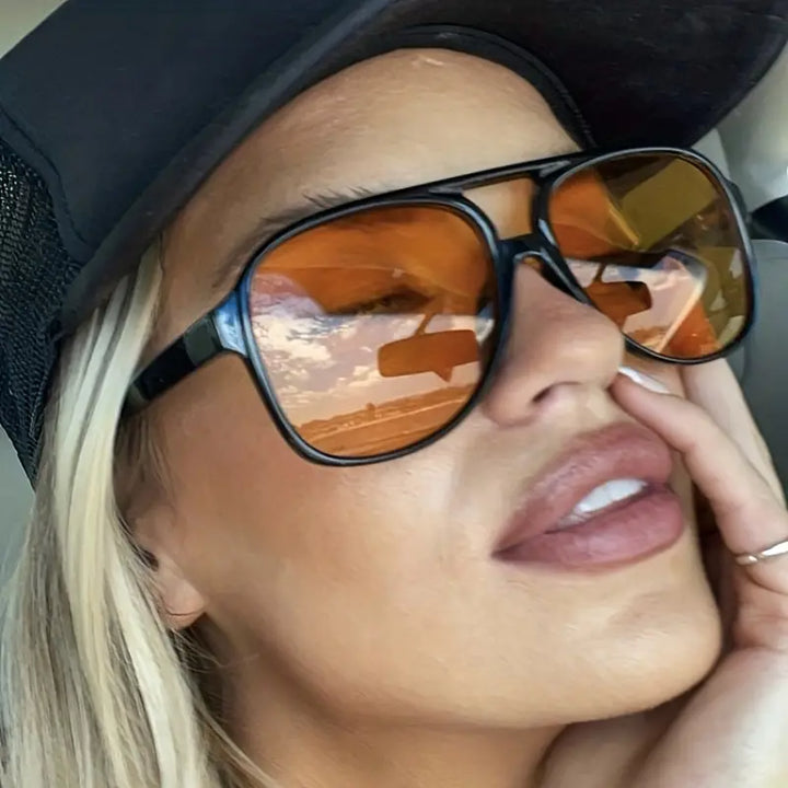 Frau mit schwarzer Kappe und orange getönten Sonnenbrillen im Auto.