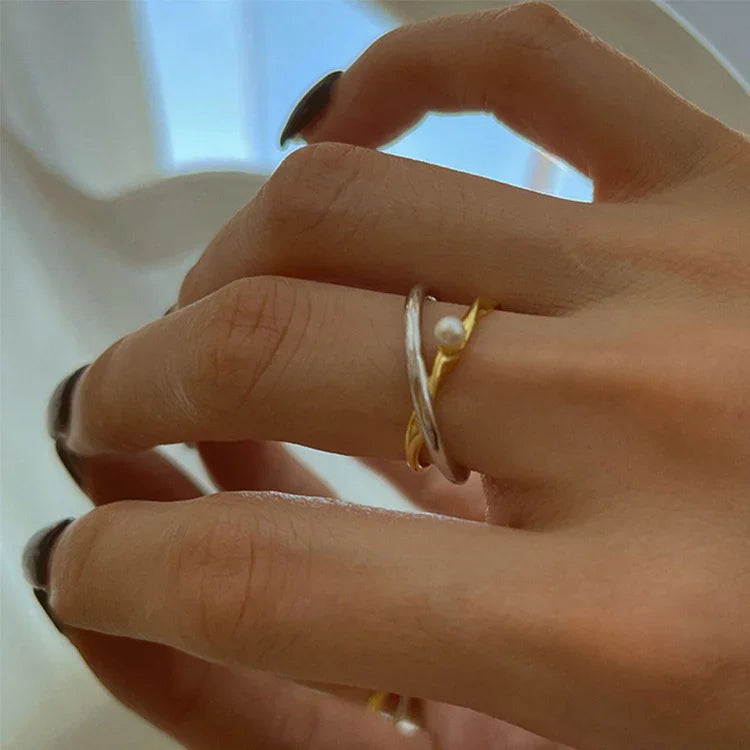 Hand mit silbernem und goldenem Ring, Perle, eleganter Schmuck, Nahaufnahme, stilvoll.