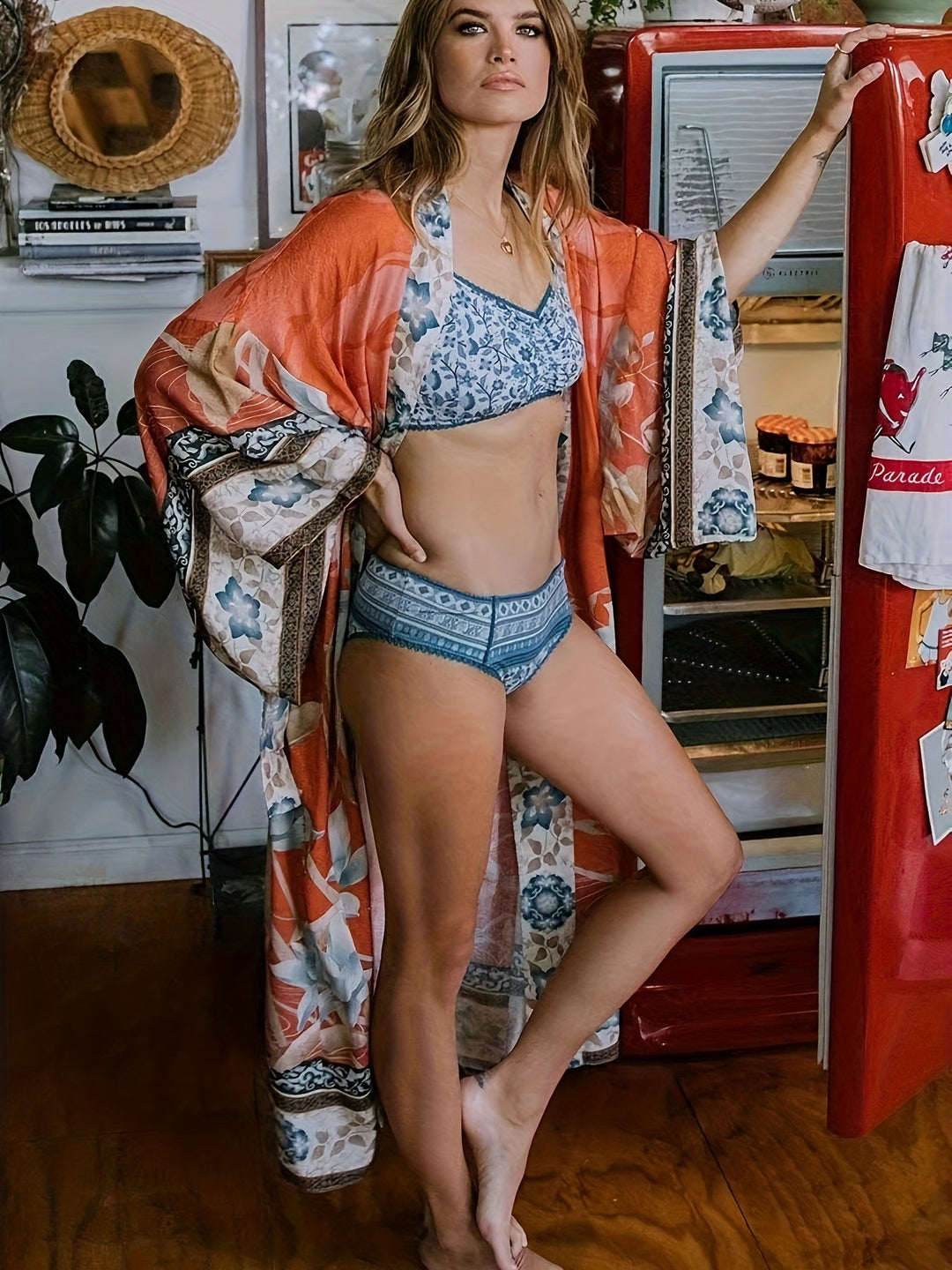 Frau in blauer Unterwäsche und rotem Kimono vor rotem Retro-Kühlschrank in Küche.