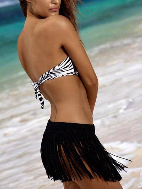 Frau am Strand in schwarz-weißem Bikini-Oberteil und schwarzem Fransenrock, Sommermode.