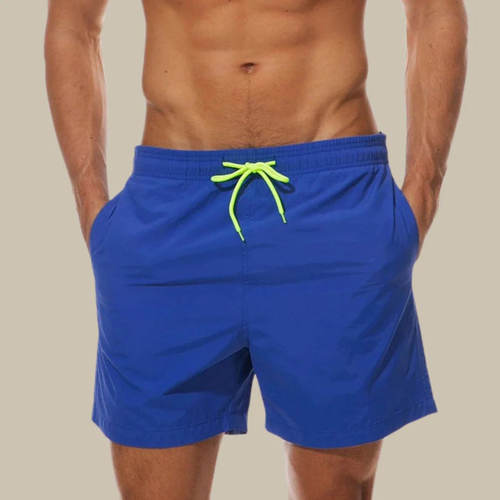 Mann in blauer Badehose mit neon-grünem Kordelzug, Strandmode, Sommerbekleidung.