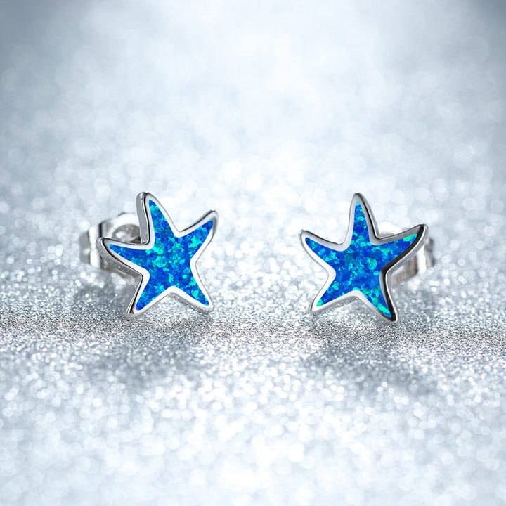 Blaue Stern-Ohrringe aus Silber mit Opal-Effekt auf glitzerndem Hintergrund.