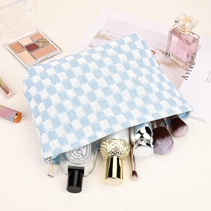 Hellblau-weiß karierte Kosmetiktasche mit Make-up-Pinseln und Parfümflasche auf hellem Hintergrund.
