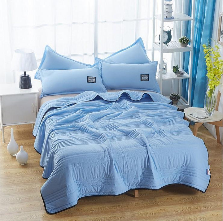 Bett mit hellblauer Bettwäsche, Kissen und Decke, modernes Schlafzimmer, Tageslicht.