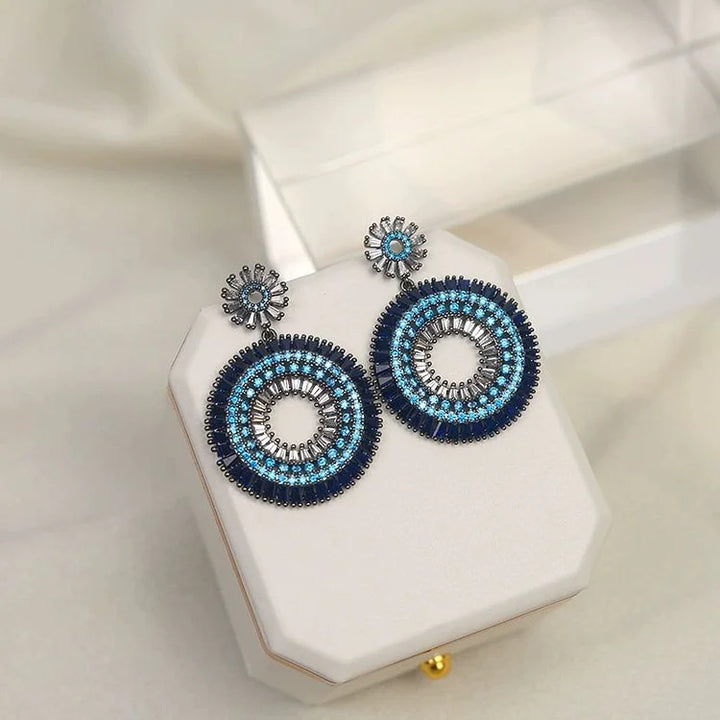 Blaue runde Ohrringe mit Perlen auf weißem Schmuckkästchen, elegantes Design, Damenaccessoire.