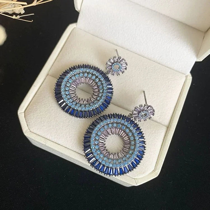Blaue runde Ohrringe mit Kristallen in Schmuckschatulle, elegantes Design, Damenaccessoire.
