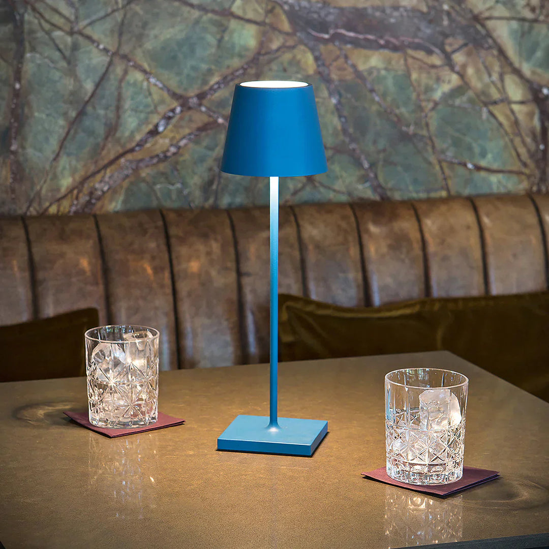 Blaue Tischlampe aus Metall auf Tisch mit zwei Kristallgläsern, stilvolle Beleuchtung.